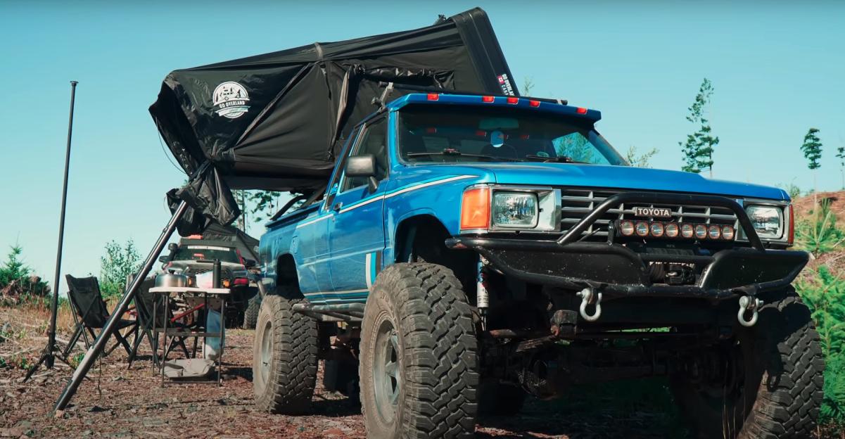 Blue pickup truck with rooftop tent and camping gear.