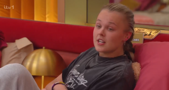 Young woman sitting on a red couch, speaking.