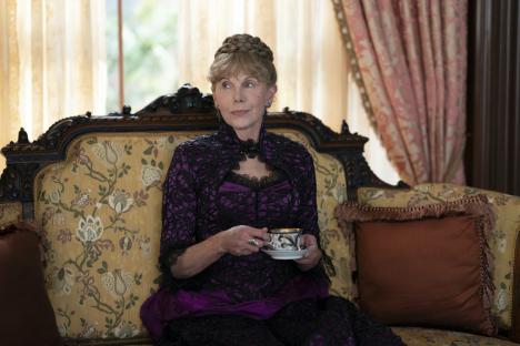 Peggy Scott, an aspiring writer in HBO's *The Gilded Age*, sits on a Victorian-style sofa holding a teacup.