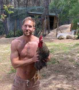 Shirtless man holding a rooster.