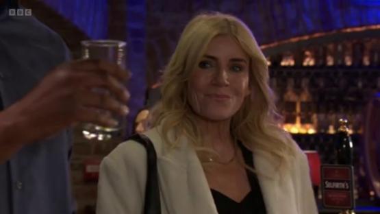 A blonde woman in a white coat at a bar.