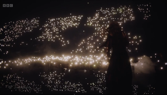 Silhouette of a person performing on stage surrounded by a crowd holding up lights.