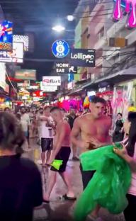 A shirtless man being helped by a woman in a crowded Pattaya street at night.