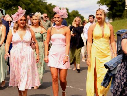 Women in dresses and hats at an outdoor event.