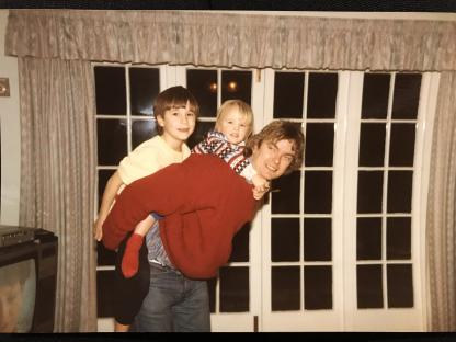 Photo of a man carrying two young children on his back.