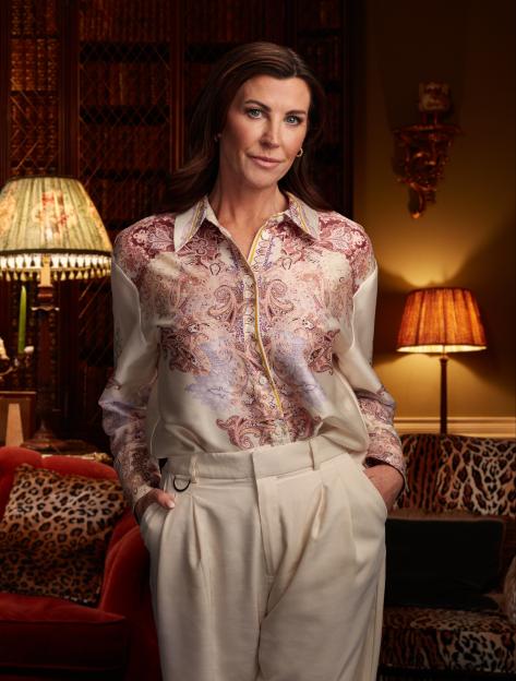 Portrait of a woman in a patterned shirt and cream trousers.