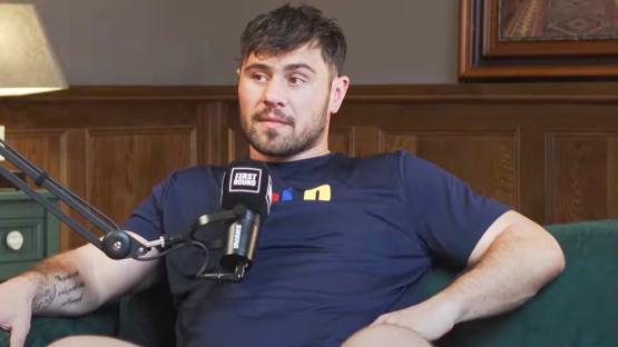 Man sitting on a couch, being interviewed with a microphone.