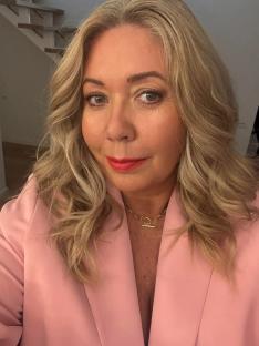 Woman in pink blazer and gold necklace.
