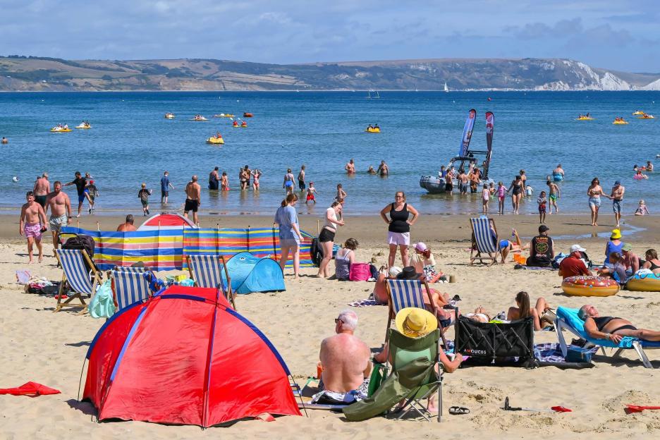 Crowded beach with people swimming, sunbathing, and relaxing in the sand.