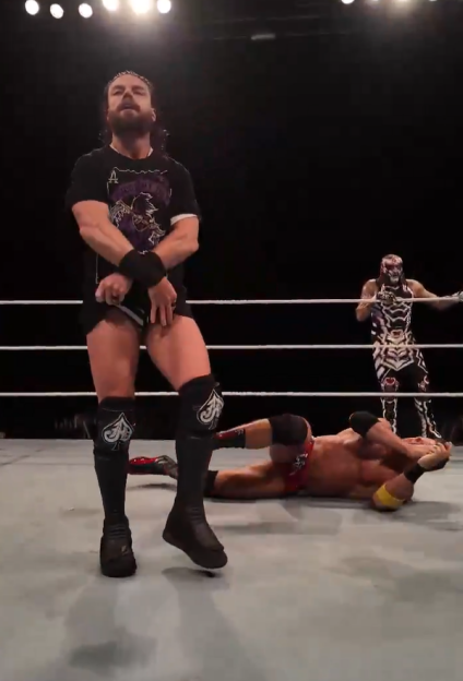 Wrestler standing over a fallen opponent in a wrestling ring.