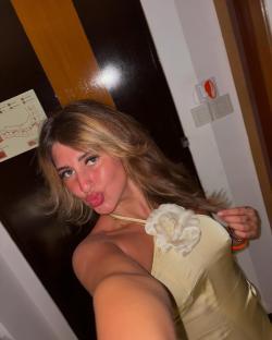 Selfie of a woman pursing her lips, wearing a pale yellow halter top.