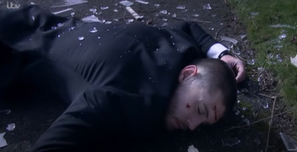 Man lying unconscious on the ground surrounded by broken glass.