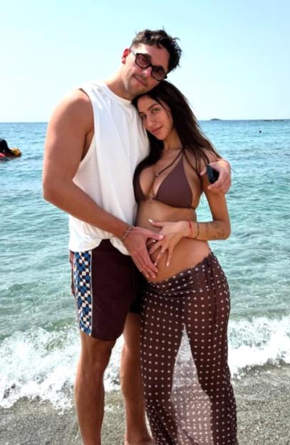 Sam Klein and his pregnant partner on a beach.