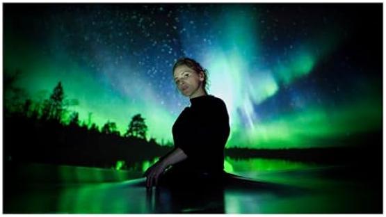 Film still of a woman sitting in water with a projected aurora borealis behind her.