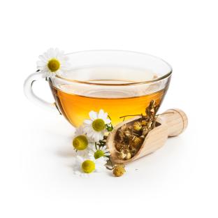 Chamomile tea in a glass cup with chamomile flowers and dried chamomile in a wooden scoop.