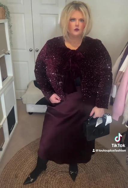 A plus-size woman models a burgundy sequined jacket over a matching silk slip dress and black pointed-toe flats.