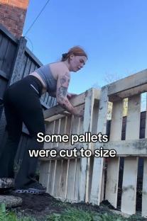 Person building a fence from wooden pallets.