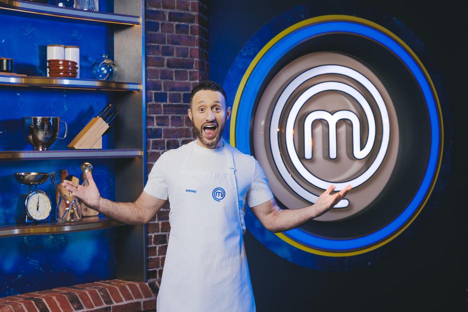 Antony in a MasterChef apron stands in front of the MasterChef logo.