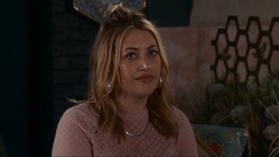 Screenshot of a woman with blonde hair wearing a pink sweater.