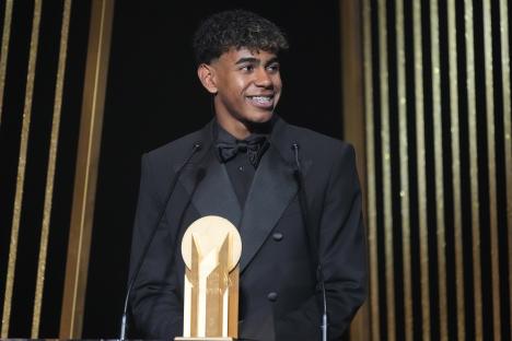 a man in a tuxedo stands at a podium with a trophy in front of him