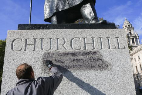 A worker cleans graffiti from the base of a Winston Churchill statue.