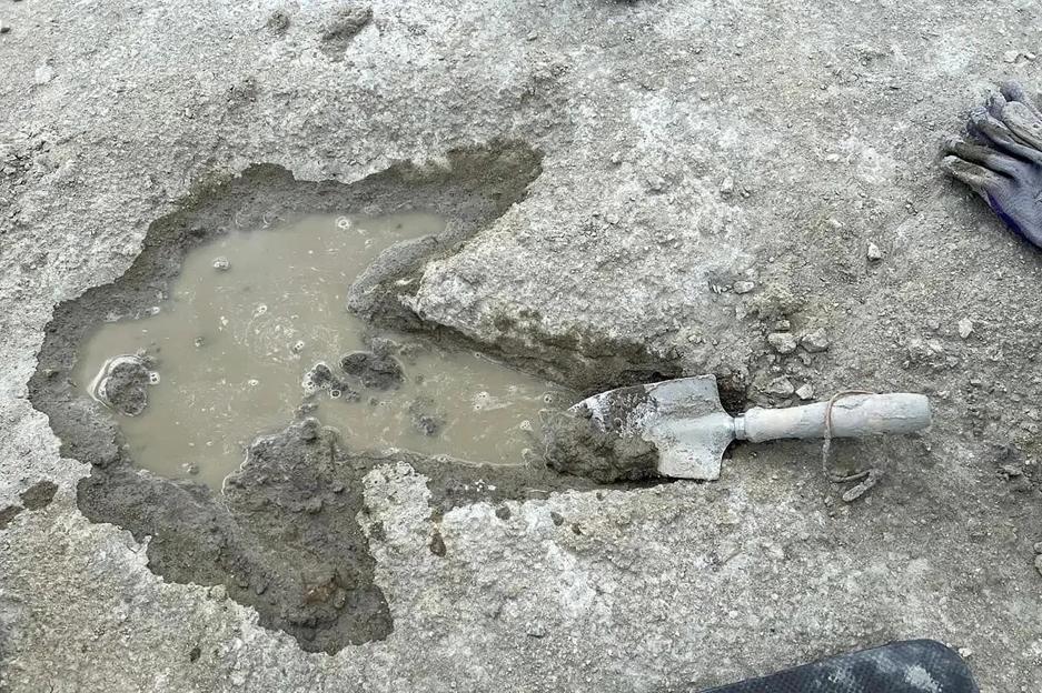 Dinosaur footprint filled with muddy water, with a small shovel resting inside it.