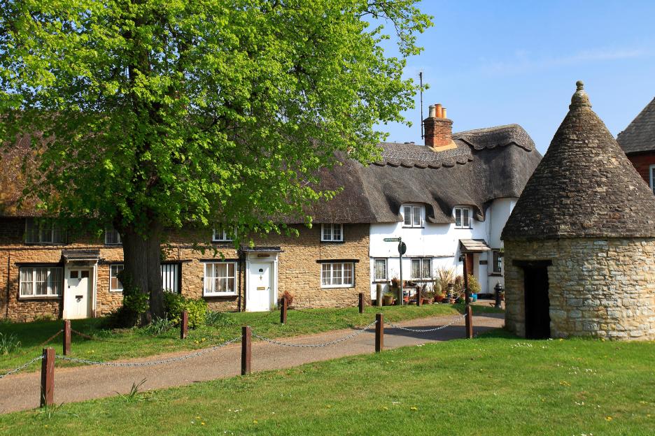 The village green at Harrold village, Bedfordshire County, England, with traditional stone and thatched-roof cottages and a conical stone structure.