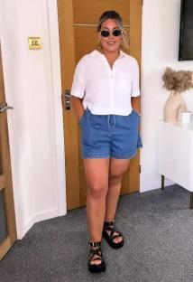 Woman wearing denim shorts, white shirt, and sandals.