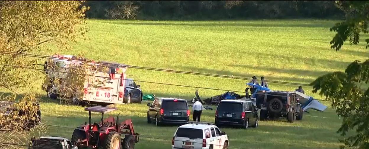 First responders at the scene of a plane crash in a grassy field.