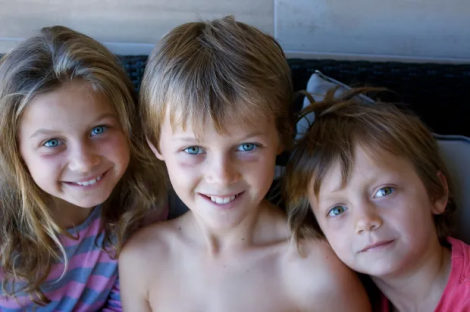 Three children smiling for a close-up photo.