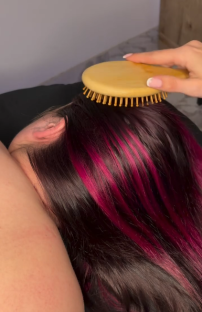 Brushing long dark hair with pink highlights using a round wooden brush.