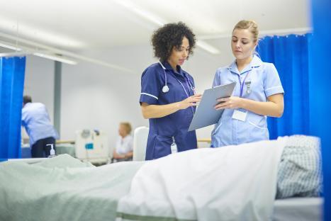 Two nurses reviewing patient notes on a hospital ward.