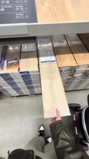 Person holding a package of light-colored laminate flooring in a store.
