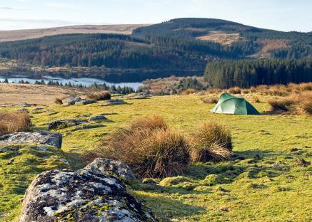 Green tent pitched in grassy field overlooking a reservoir.
