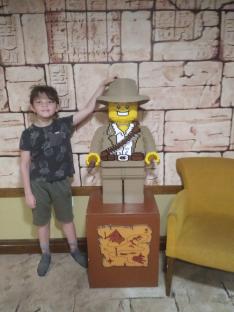 Boy standing next to a large Lego adventurer figure.