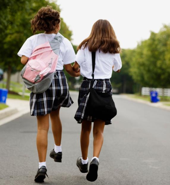 Two schoolgirls holding hands and walking down a street.
