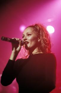 a woman singing into a microphone with a pink background