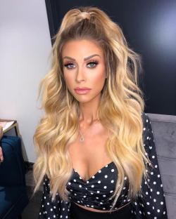 Woman with long blonde wavy hair in a half-updo, wearing a black and white polka dot top.