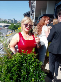 Woman in red sequined dress holding a champagne glass on a balcony overlooking a city.