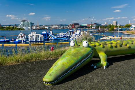 Inflatable aqua park with children playing, and a large crocodile statue in the foreground.