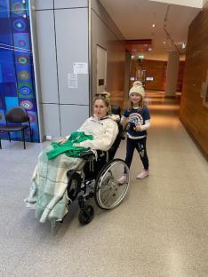 Woman in wheelchair with young girl in hospital hallway.