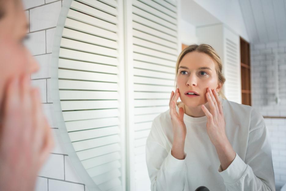 Skin analysis in mirror. Focused woman examines her face for signs of aging and wrinkles in bathroom