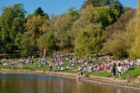 Crowds of people sunbathing by a lake in Hampstead Heath, London.