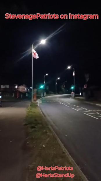 Nighttime photo of a road with a flagpole displaying a flag.