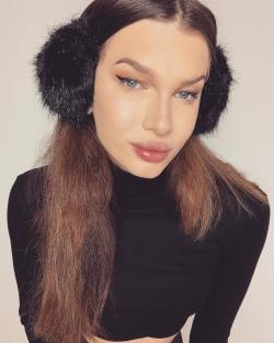 Woman with long brown hair wearing black earmuffs and a black turtleneck.
