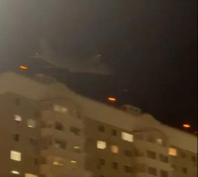 A military jet flies low over a building at night.