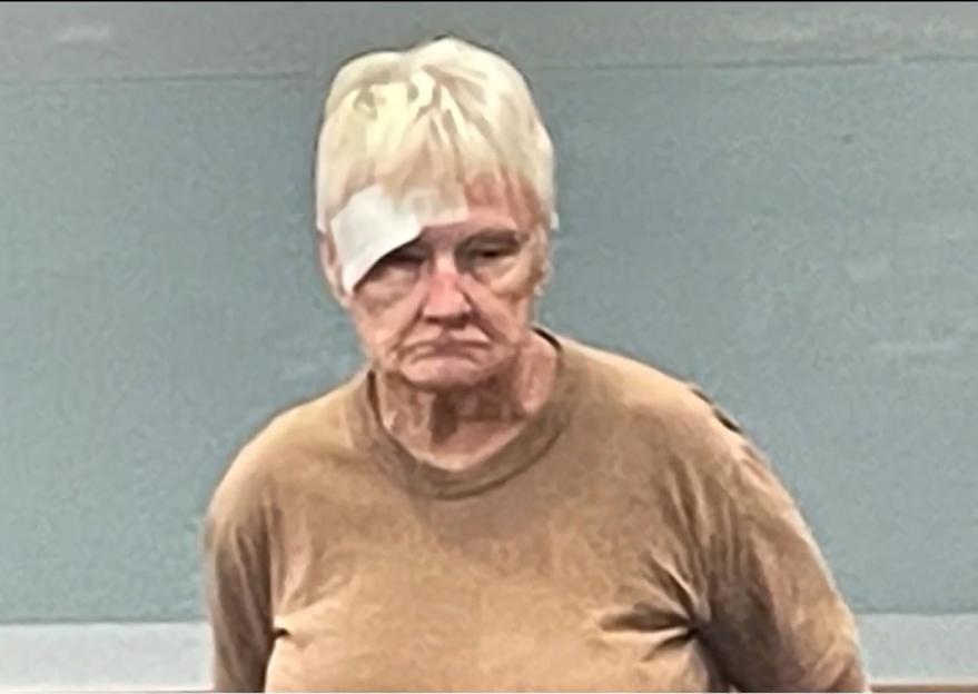 Mugshot of a 76-year-old woman with a bandage on her forehead.