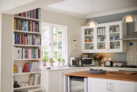 Bright kitchen interior with white cabinets, a bookshelf filled with books, and kitchen appliances.
