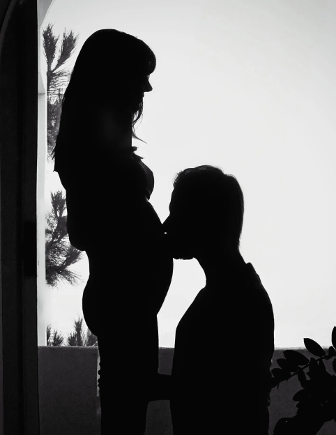 Silhouette of a man kissing a pregnant woman's belly.