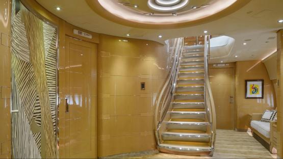 Interior of a luxurious private jet, showing a staircase and gold-toned walls.